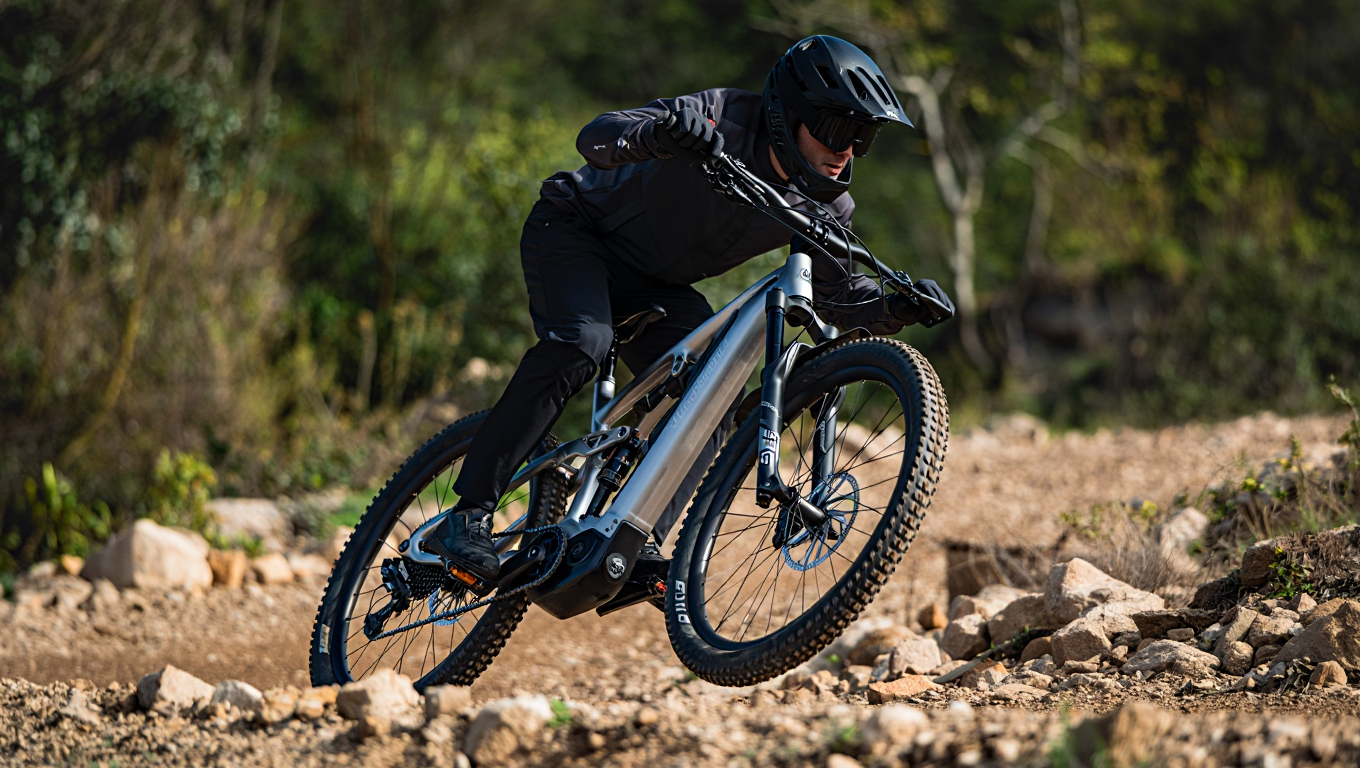 An electric mountain bike with full suspension navigating a rocky trail, rider wearing a helmet.